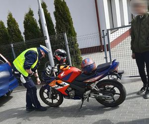 Policjant w kamizelce odblaskowej w czasie kontroli drogowej sprawdza stan techniczny motocykla.