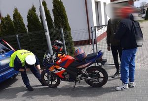 Policjant w kamizelce odblaskowej w czasie kontroli drogowej sprawdza stan techniczny motocykla.